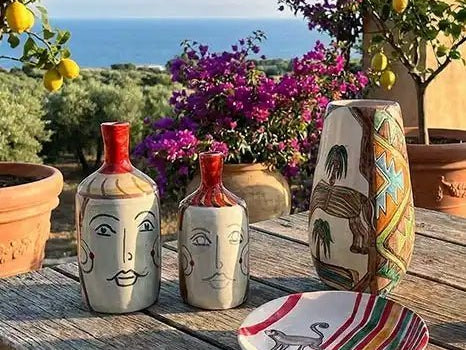 ceramiche dell'artista Artema Galli su un tavolo, in sicilia, tra piante di limoni e mare sullo sfondo