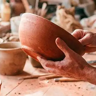mani di un artista che tiene una ciotola in terracotta nel suo laboratorio artigianale