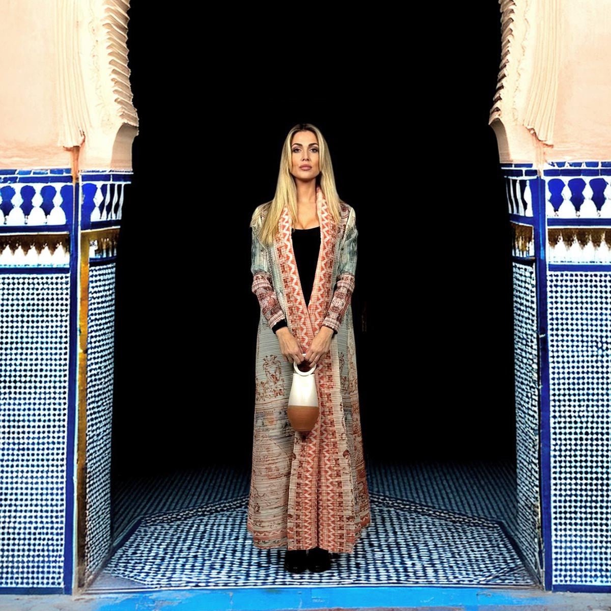 Il kimono plissettato Blush Horizon piegato accanto a una valigia aperta per mostrare la sua praticità.