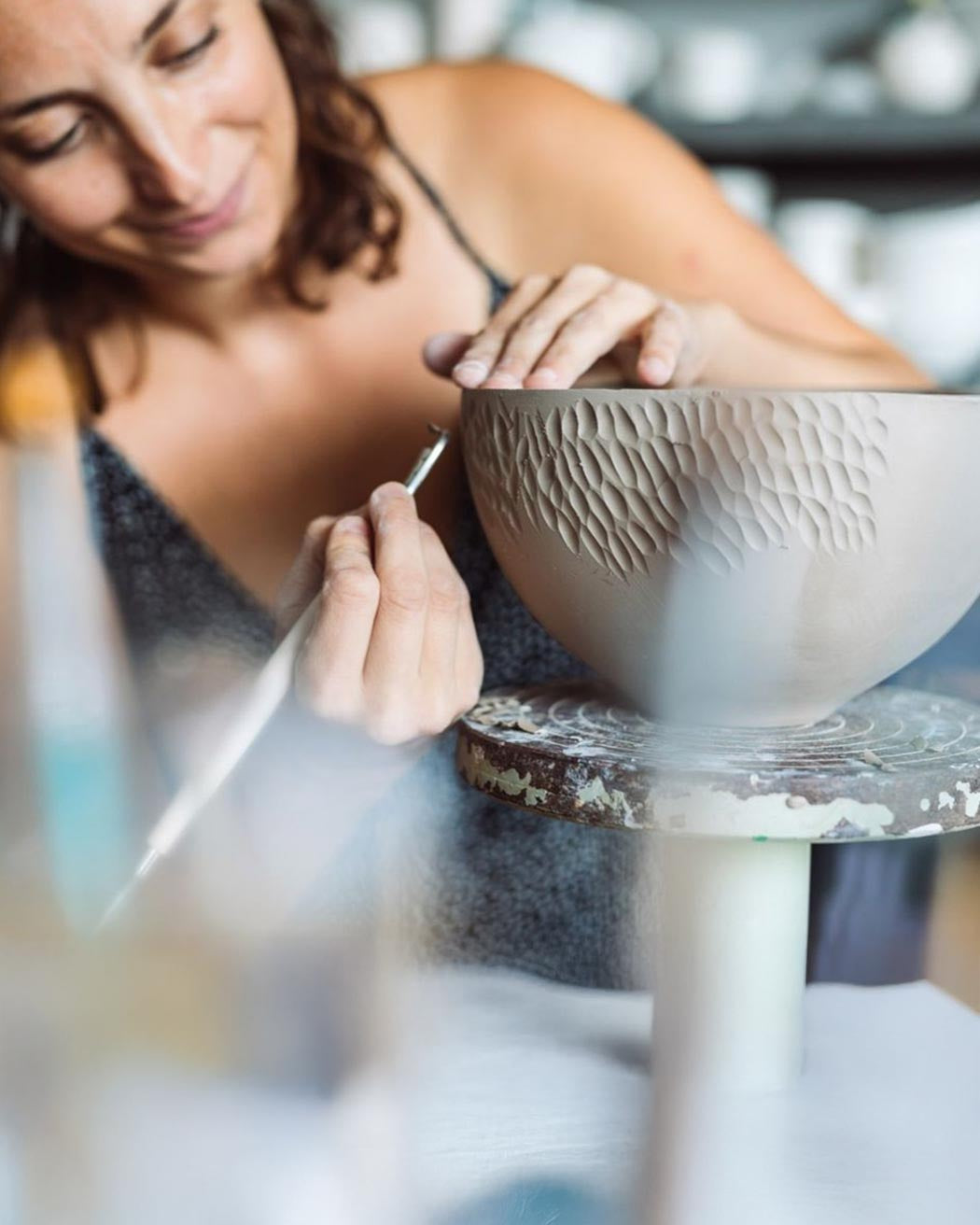 L'Artista Luana Baglì concentrata mentre incide con uno strumento di precisione la superficie di una ciotola di argilla nel suo studio.