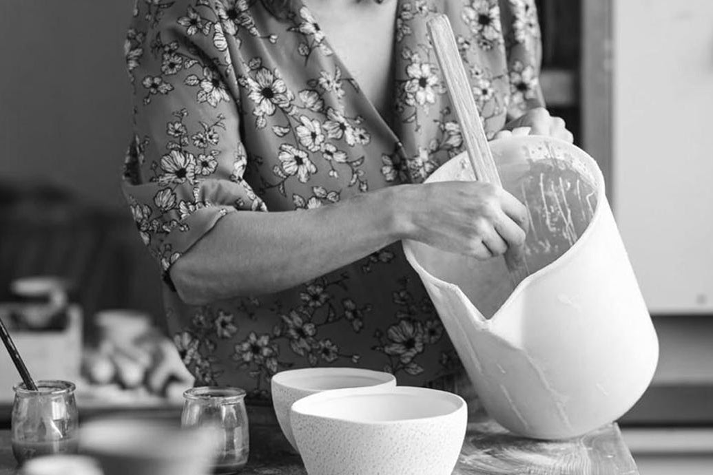 L'artista Luana Baglì che prepara con cura la materia prima in un laboratorio, mescolando un composto in un grande recipiente.