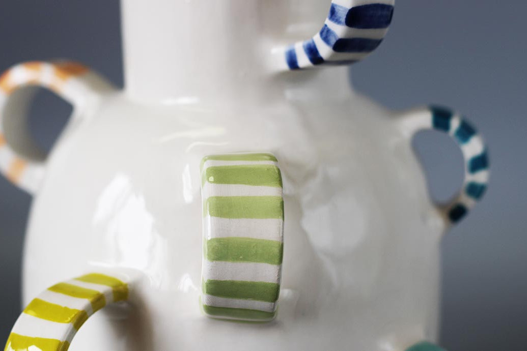 Primo piano di un vaso in ceramica finemente lavorato, con dettagli decorativi unici e manici scultorei a righe e pois.