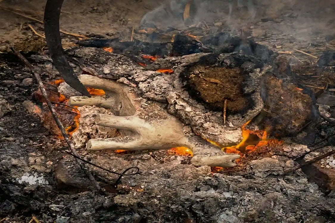 Cottura primitiva della ceramica malles a fuoco vivo all'aperto, con fiamme, braci ardenti e fumo che avvolgono i pezzi in lavorazione.
