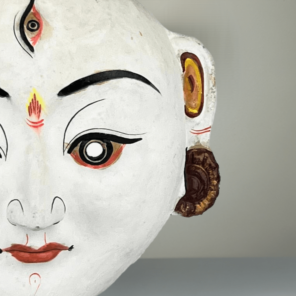Primo piano del volto intenso e dei dettagli dei gioielli finemente dipinti sulla Maschera di Durga.