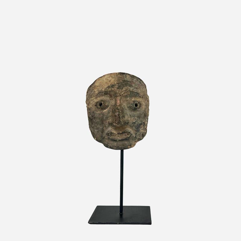 Maschera Volto Arcaico, antico manufatto mediterraneo in terracotta grezza, esposta sulla sua base in metallo.