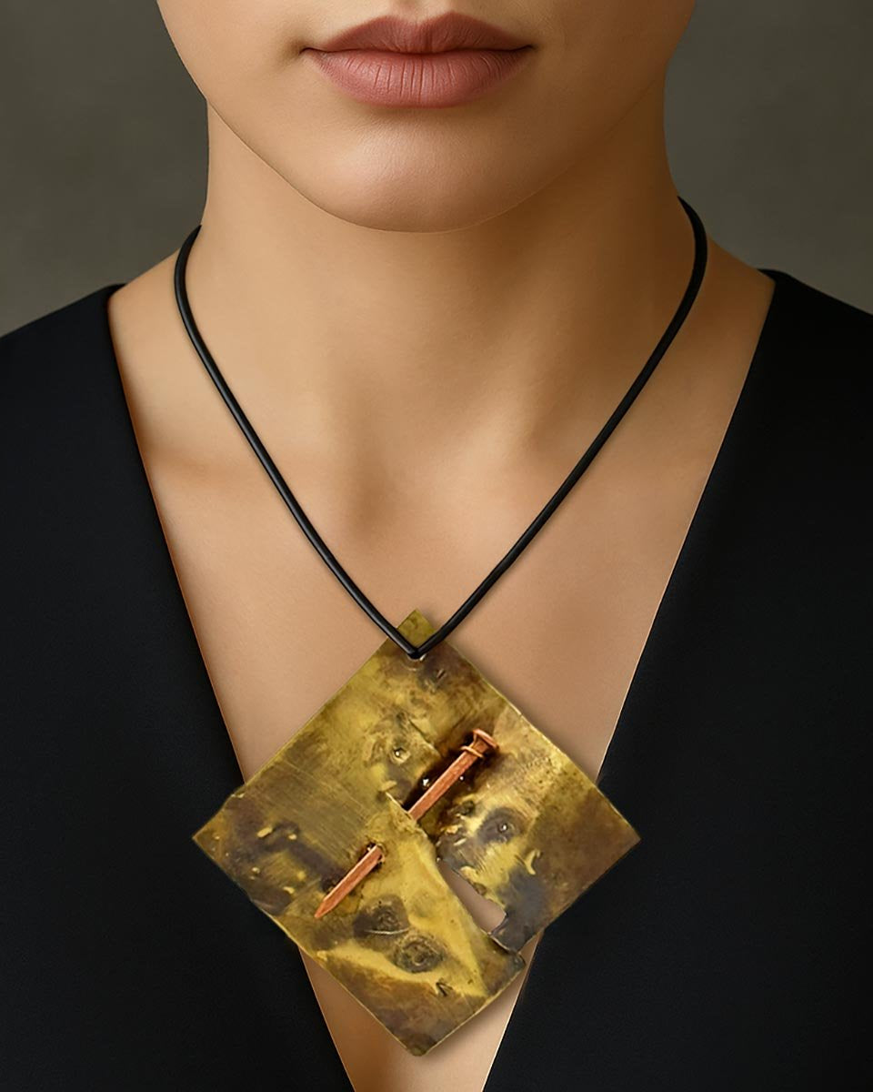 Monile Chiodo Sacrale, gioiello artigianale con placca in ottone incisa e chiodo centrale.