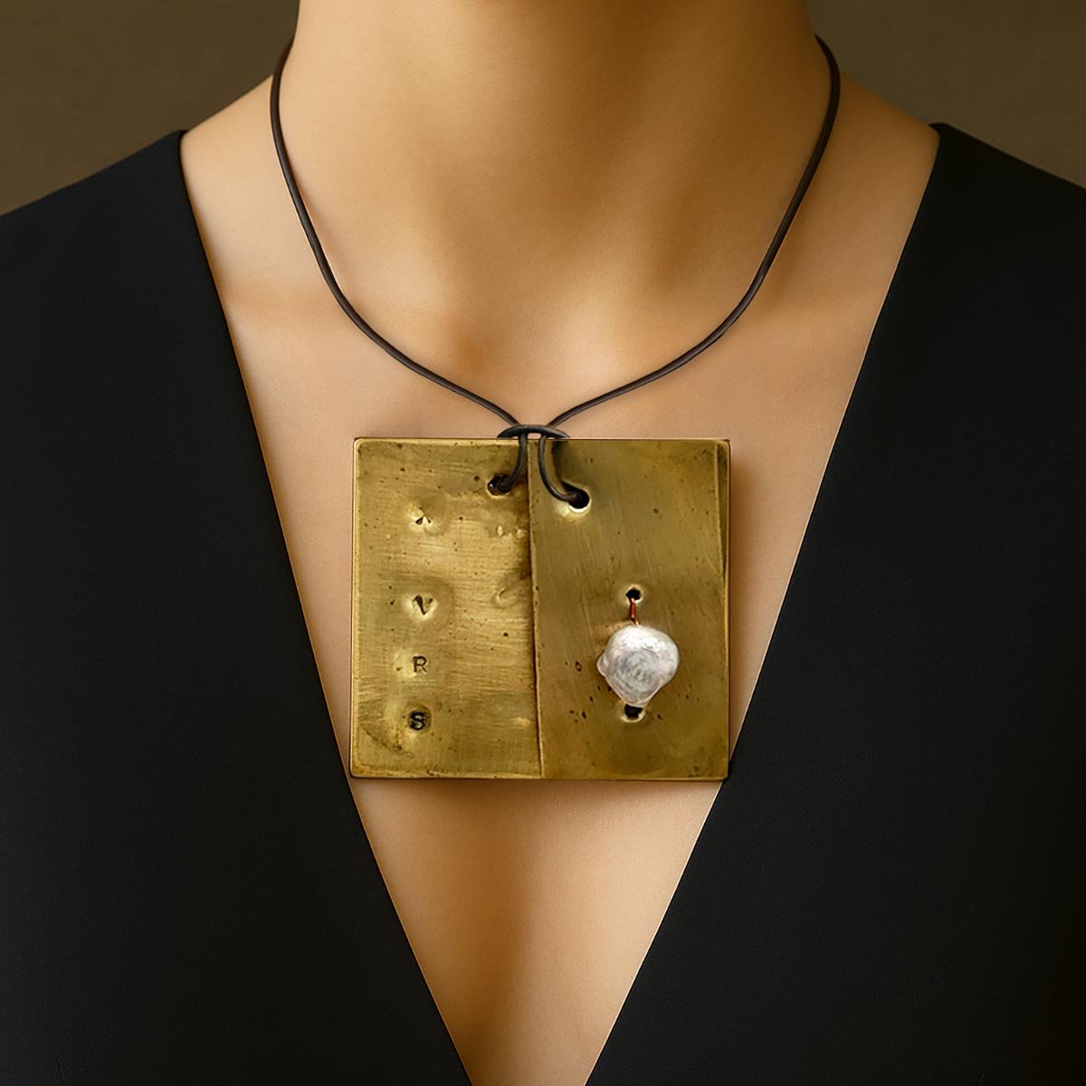 Monile Perla Nomade, gioiello artigianale con perla barocca sospesa su placca in ottone inciso.