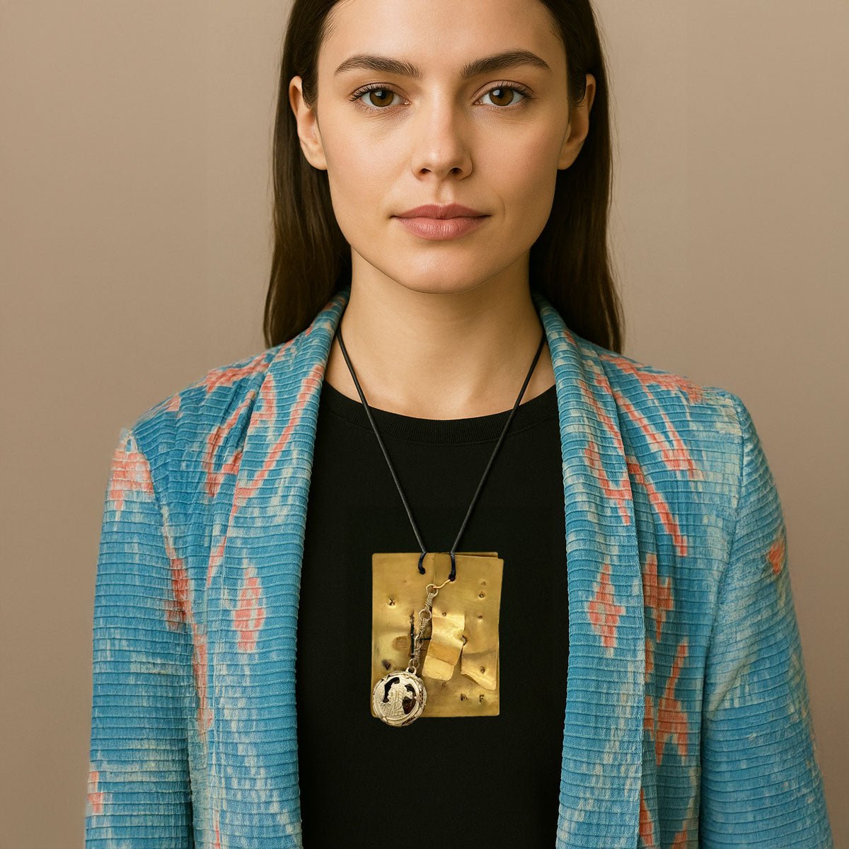 Primo piano del ciondolo con effige in stile etrusco, in metallo cesellato e corda naturale.