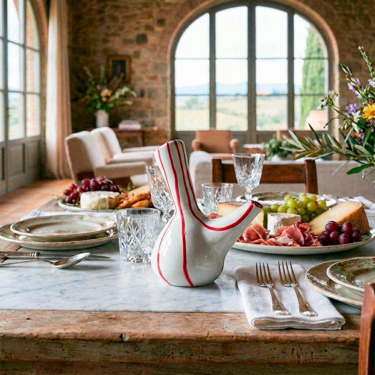 Dettaglio di una tavola rustica imbandita per un pasto festivo in una lussuosa villa toscana, con la aceteira a strisce rosse come elemento centrale tra cibo e stoviglie.