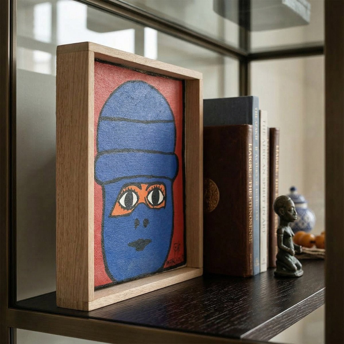 Dipinto naive marocchino di un volto blu in cornice di okoume su scaffale.