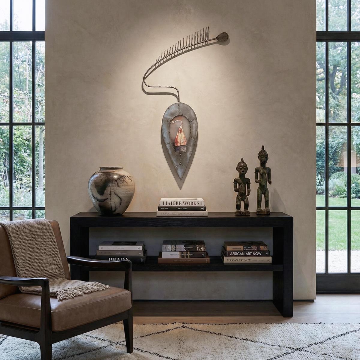 Primo piano di una scultura artistica da parete in metallo grezzo e saldato. La struttura presenta uno spessore rilevante di 10 cm, ben visibile nei bordi profondi della base ovale che incornicia un piccolo dipinto, e nel lungo braccio curvo terminante con una serie di punte. La luce laterale accentua la profondità e le ombre sulla parete materica beige.