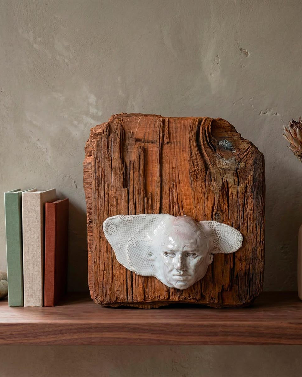 Scultura d'avanguardia con volto alato e trama a rete su supporto di legno nodoso.