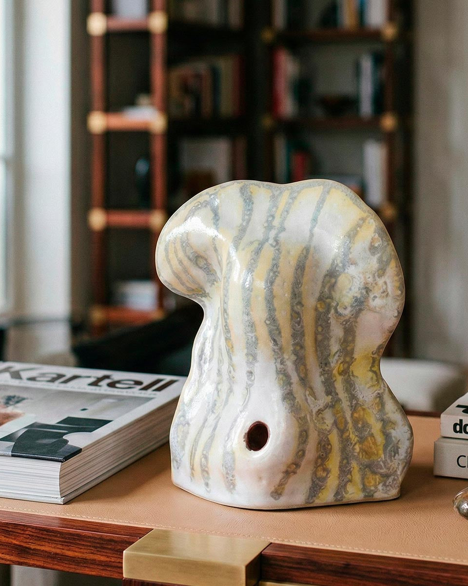 Scultura organica in ceramica con forme rigonfie e venature verticali giallo e grigio.