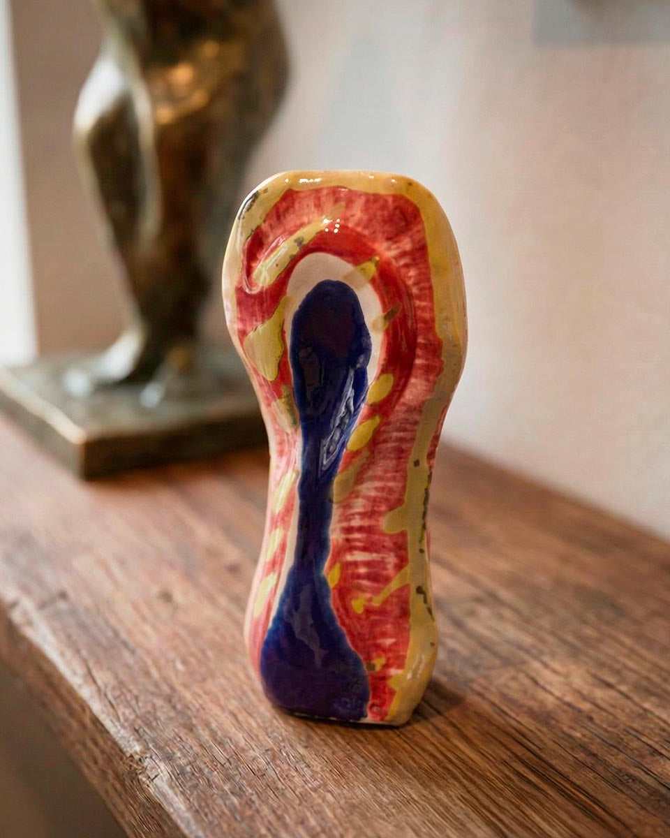 Scultura in ceramica policroma con colature blu, rosse e gialle su fondo bianco.