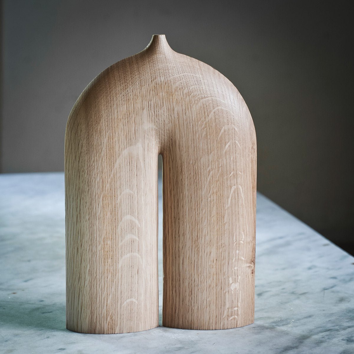 La scultura in legno di rovere esposta da sola su una mensola, mostrando la sua forma ad arco.