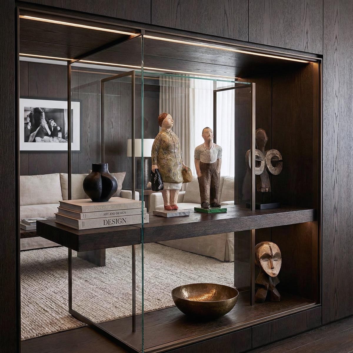 Dettaglio ravvicinato dall'alto delle due sculture in cartapesta raffiguranti un uomo e una donna. L'inquadratura mette in risalto la texture ruvida e i colori dipinti a mano dei personaggi, posizionati su una mensola in legno scuro all'interno di una teca di vetro illuminata a LED. A lato sono visibili libri d'arte e un vaso in ceramica nera.