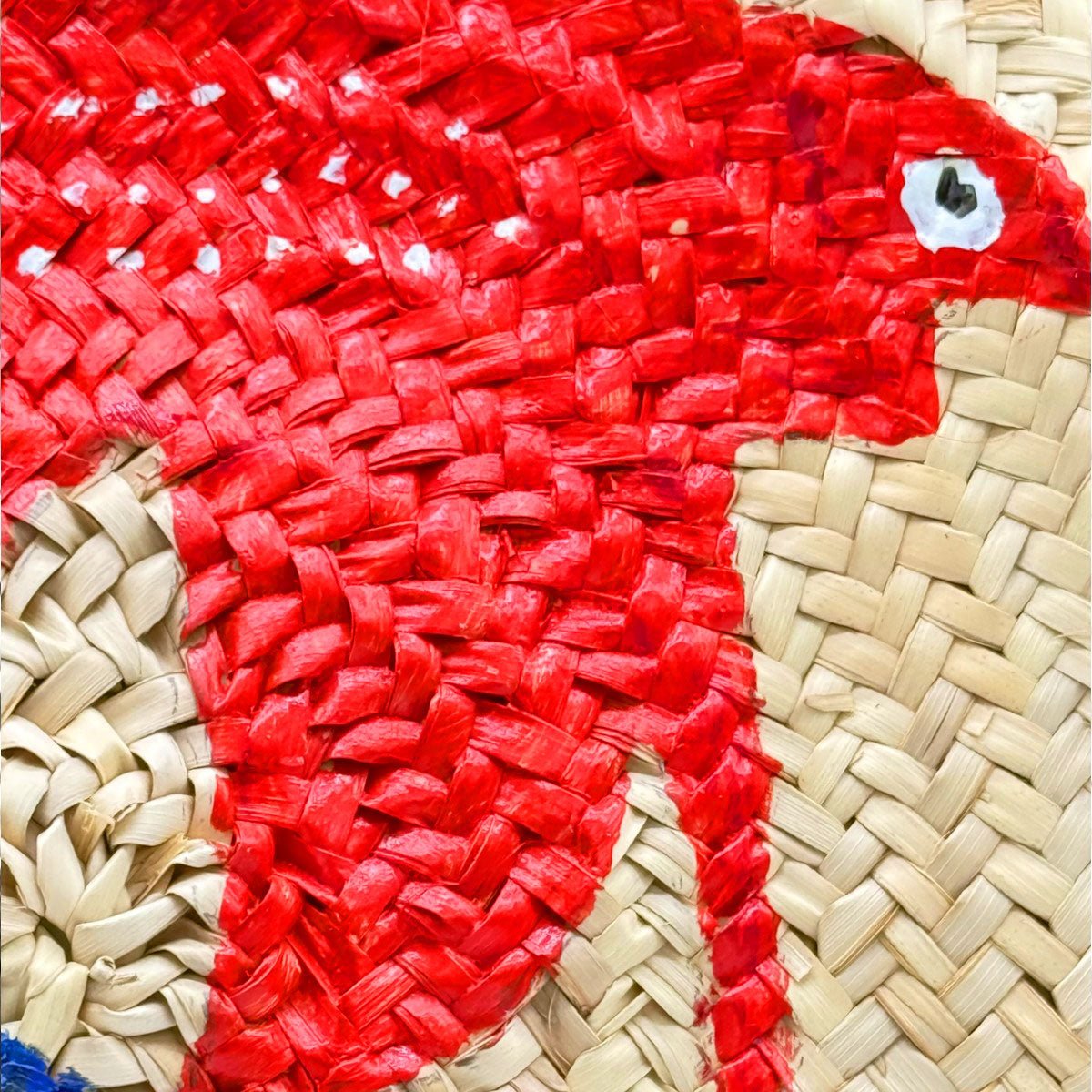 Primo piano del dipinto dei due pesci, uno rosso e uno blu, sulla borsa in paglia.