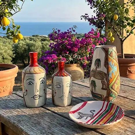 ceramiche dell'artista Artema Galli su un tavolo, in sicilia, tra piante di limoni e mare sullo sfondo