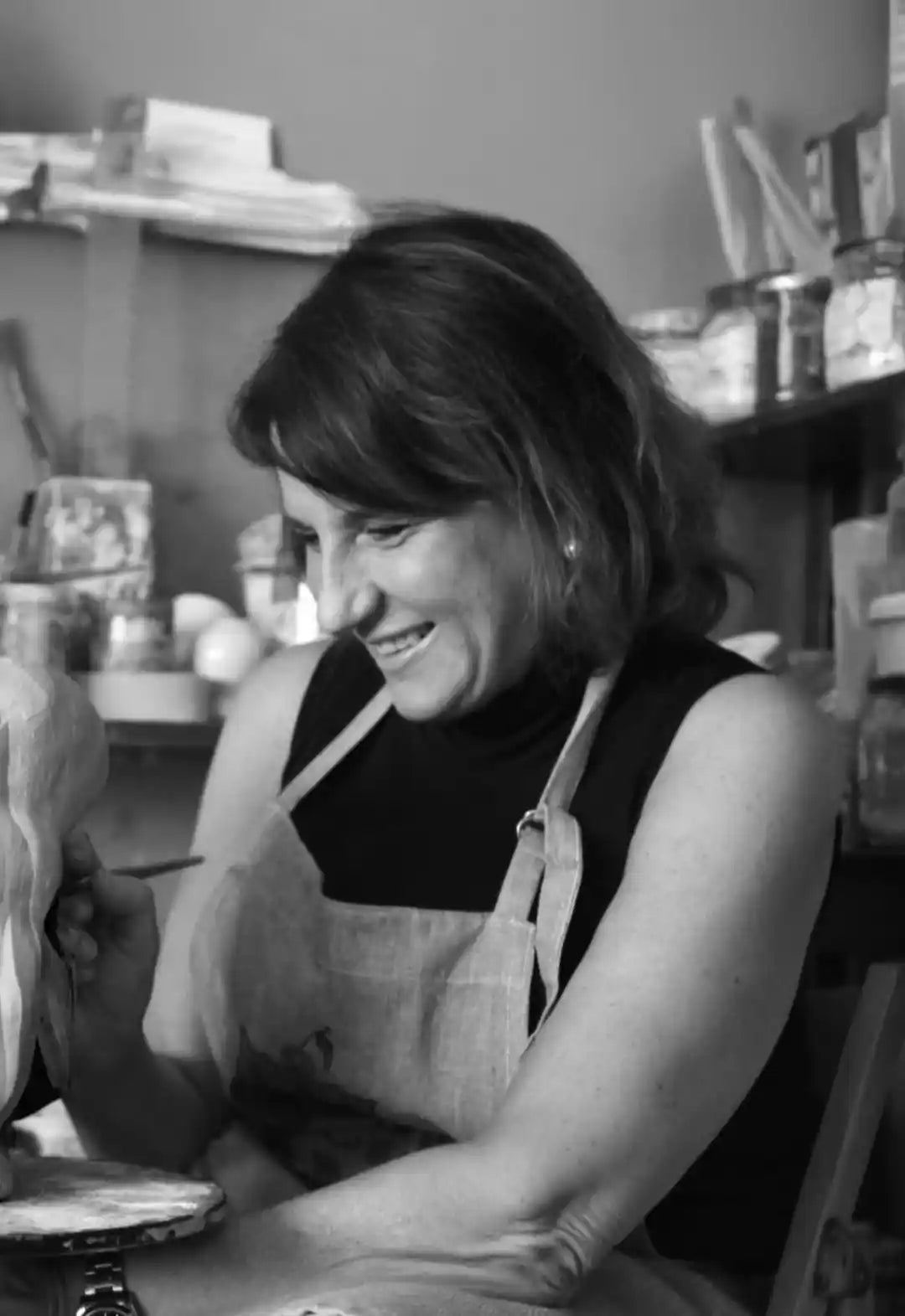 Ritratto in bianco e nero della ceramista Artema Galli sorridente mentre lavora nel suo laboratorio.