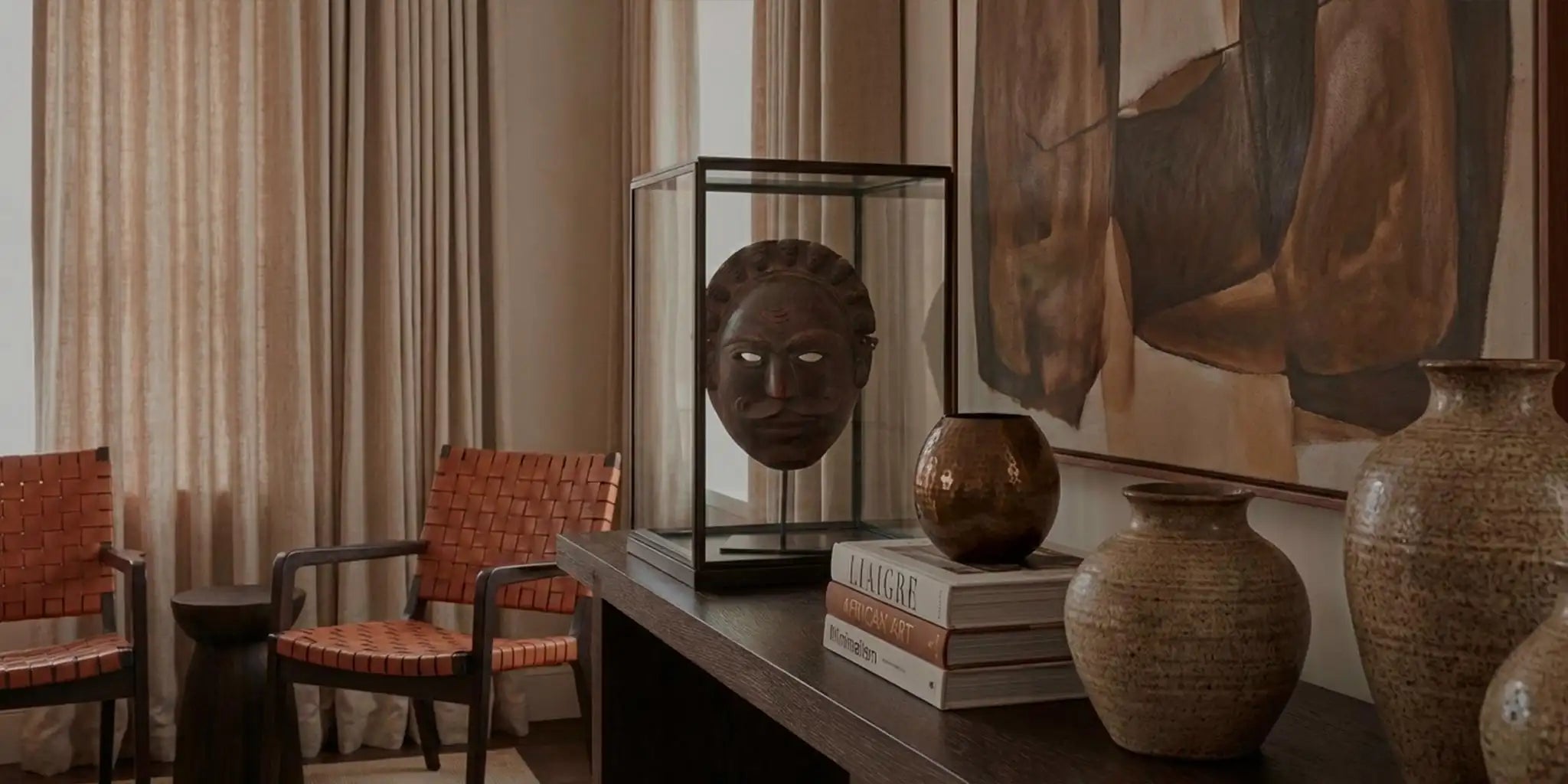 Hero banner dell'homepage Vicode per il Black Friday. L'immagine panoramica mostra un lussuoso salotto in stile Liaigre dove spicca una maschera africana antica esposta in una teca di vetro su una console di legno scuro, circondata da vasi in ceramica testurizzata, libri d'arte e poltrone in pelle intrecciata. L'atmosfera calda evoca l'artigianato unico in offerta.