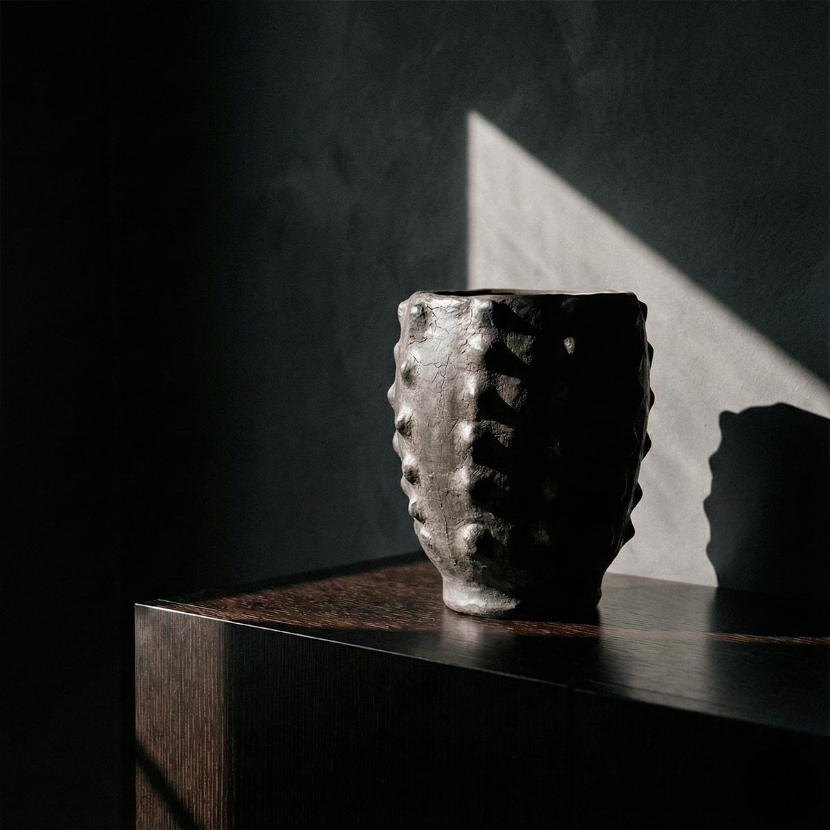 Calice Nero Scolpito su credenza in legno scuro con luce radente collezione Malles x Vicode.