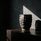 Calice Nero Scolpito su credenza in legno scuro con luce radente collezione Malles x Vicode.