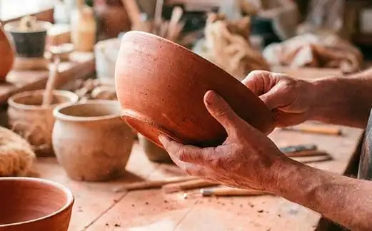 mani di un artista che tiene una ciotola in terracotta nel suo laboratorio artigianale