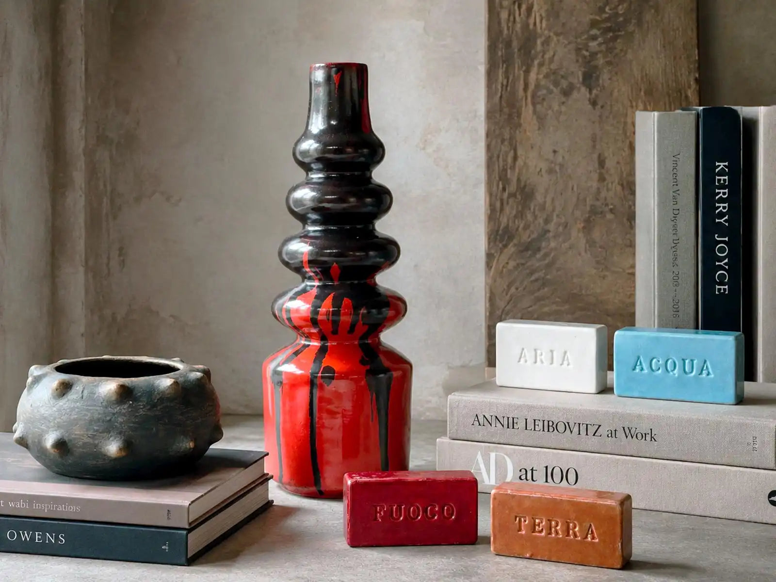 Composizione decorativa con vaso alto libri ceramica e piccola scultura disposti su un piano neutro
