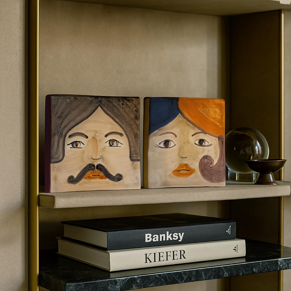 Le mattonelle ceramica dipinte Idda & Iddu usate come fermalibri su una mensola.