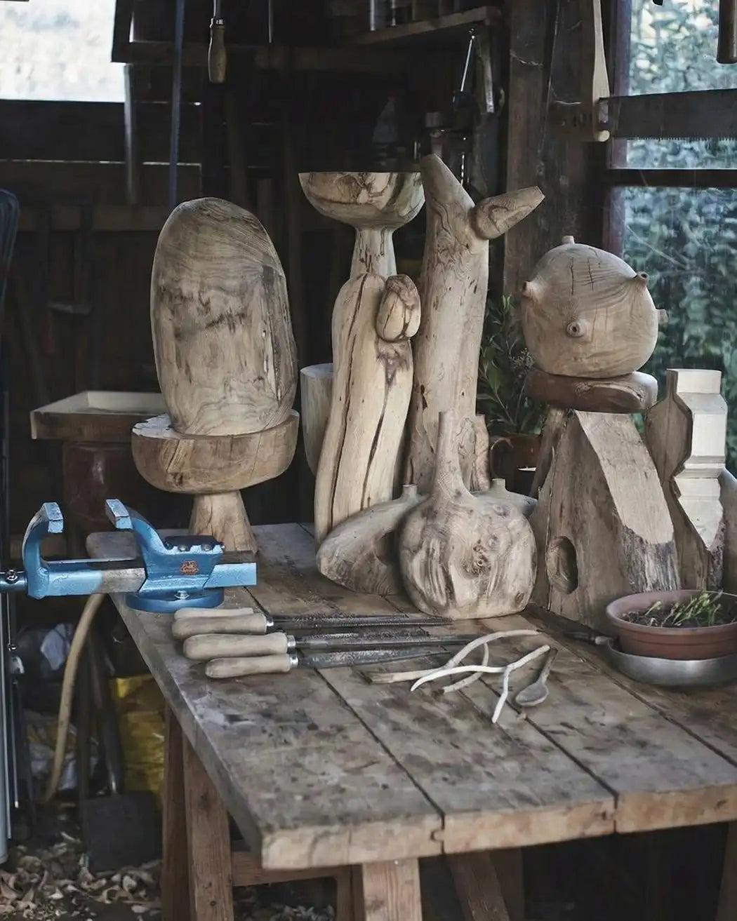 Tavolo da lavoro di Estebanland con sculture in legno grezzo e attrezzi da intaglio sparsi.