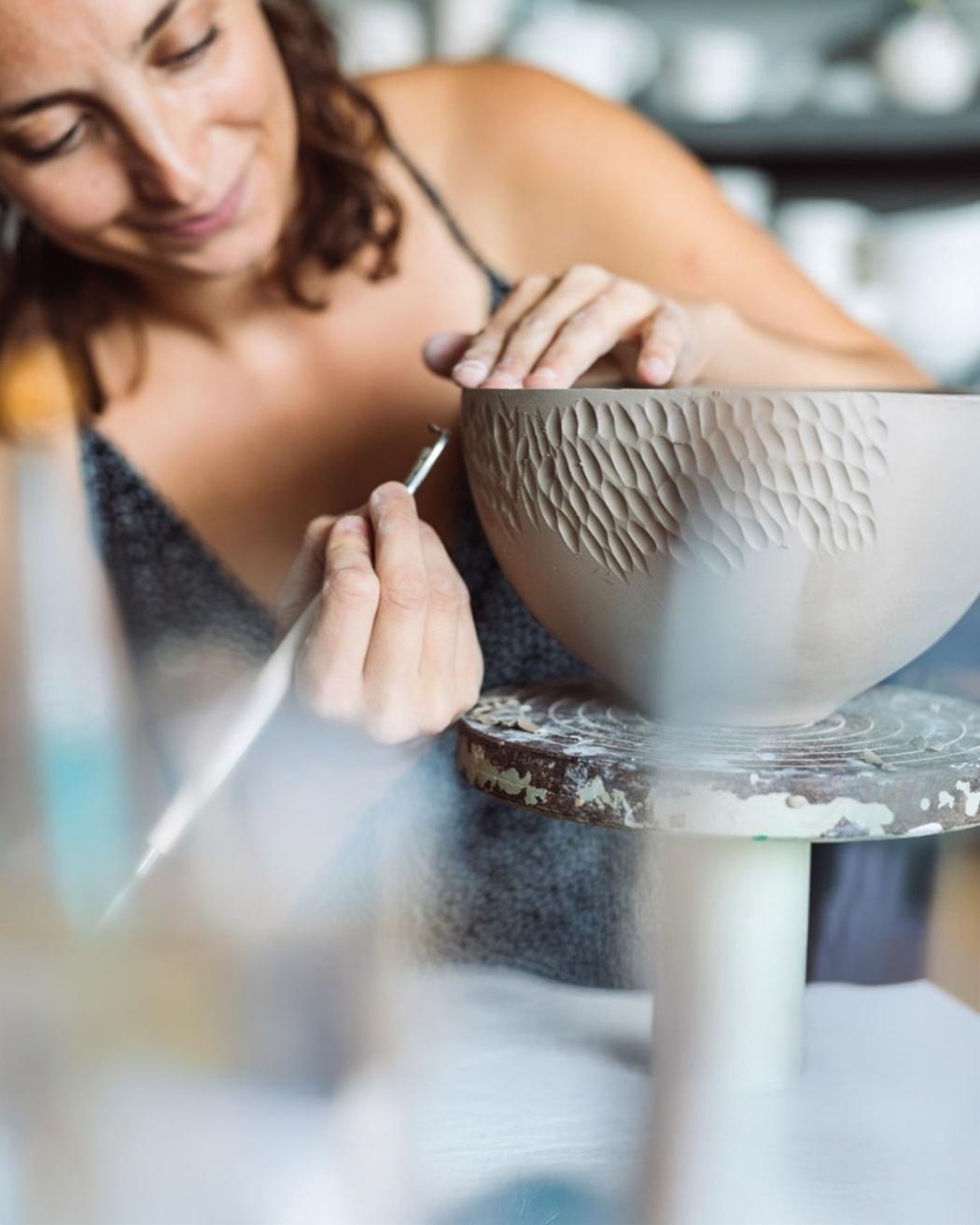 L'Artista Luana Baglì concentrata mentre incide con uno strumento di precisione la superficie di una ciotola di argilla nel suo studio.