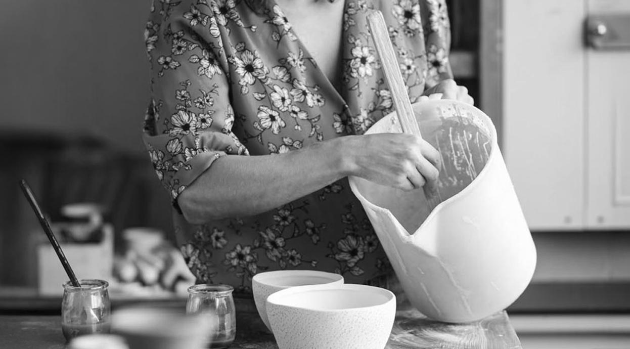 L'artista Luana Baglì che prepara con cura la materia prima in un laboratorio, mescolando un composto in un grande recipiente.
