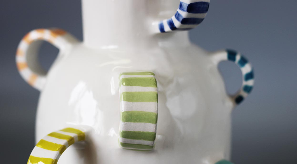 Primo piano di un vaso in ceramica finemente lavorato, con dettagli decorativi unici e manici scultorei a righe e pois.