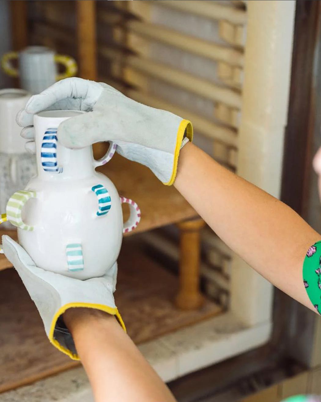 Mani protette da guanti che sorreggono con delicatezza un vaso artistico in ceramica bianca con dettagli colorati.