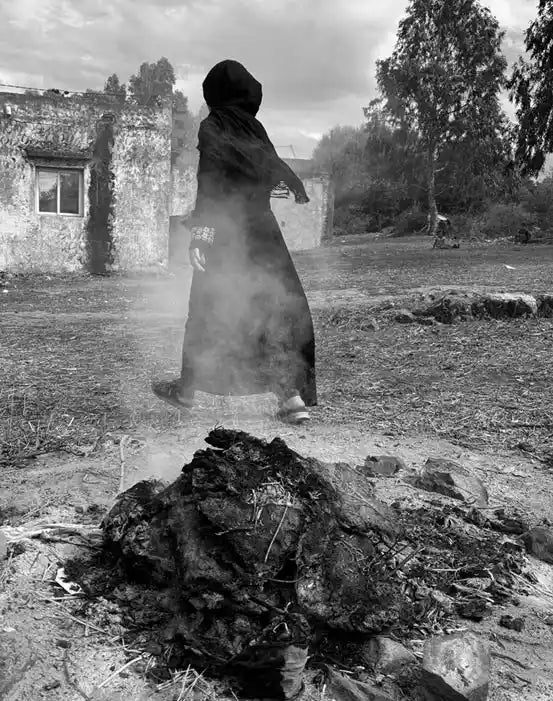 fotografia artistica in bianco e nero che ritrae una donna tunisina in abiti tradizionali vicino a un fuoco di cottura della ceramica malles in un ambiente rurale.