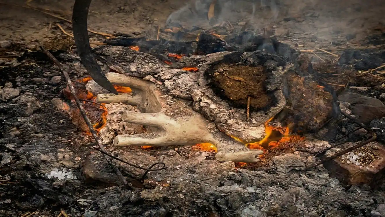 Cottura primitiva della ceramica malles a fuoco vivo all'aperto, con fiamme, braci ardenti e fumo che avvolgono i pezzi in lavorazione.