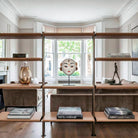 Sofisticata zona living di un appartamento londinese dallo stile contemporaneo. Su un'elegante libreria con struttura in metallo bronzato e ripiani rivestiti in pelle color biscotto, è esposta una maschera rituale di Durga in cartapesta su piedistallo, armoniosamente circondata da libri di design e oggetti d'arte in un contesto stile Poliform.