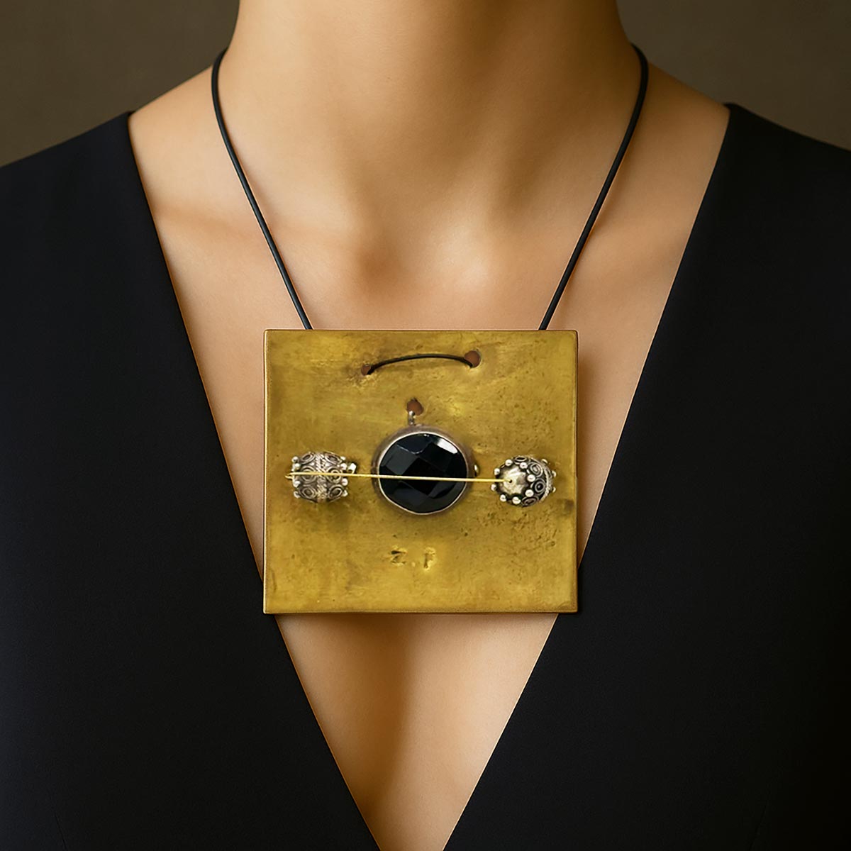 Monile Eclissi Errante, gioiello artigianale con placca in ottone e pietra nera sfaccettata.