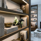 Scultura artistica in ceramica smaltata raffigurante due cavalli che si impennano (uno marmorizzato giallo-verde, uno nero), esposta come pezzo centrale su una libreria in legno scuro in stile Liaigre. L'illuminazione a LED integrata esalta la texture lucida della ceramica, circondata da libri di design, una ciotola in bronzo martellato e una maschera etnica in un salotto sofisticato.