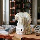 Scultura organica in ceramica con forme rigonfie e venature verticali giallo e grigio.
