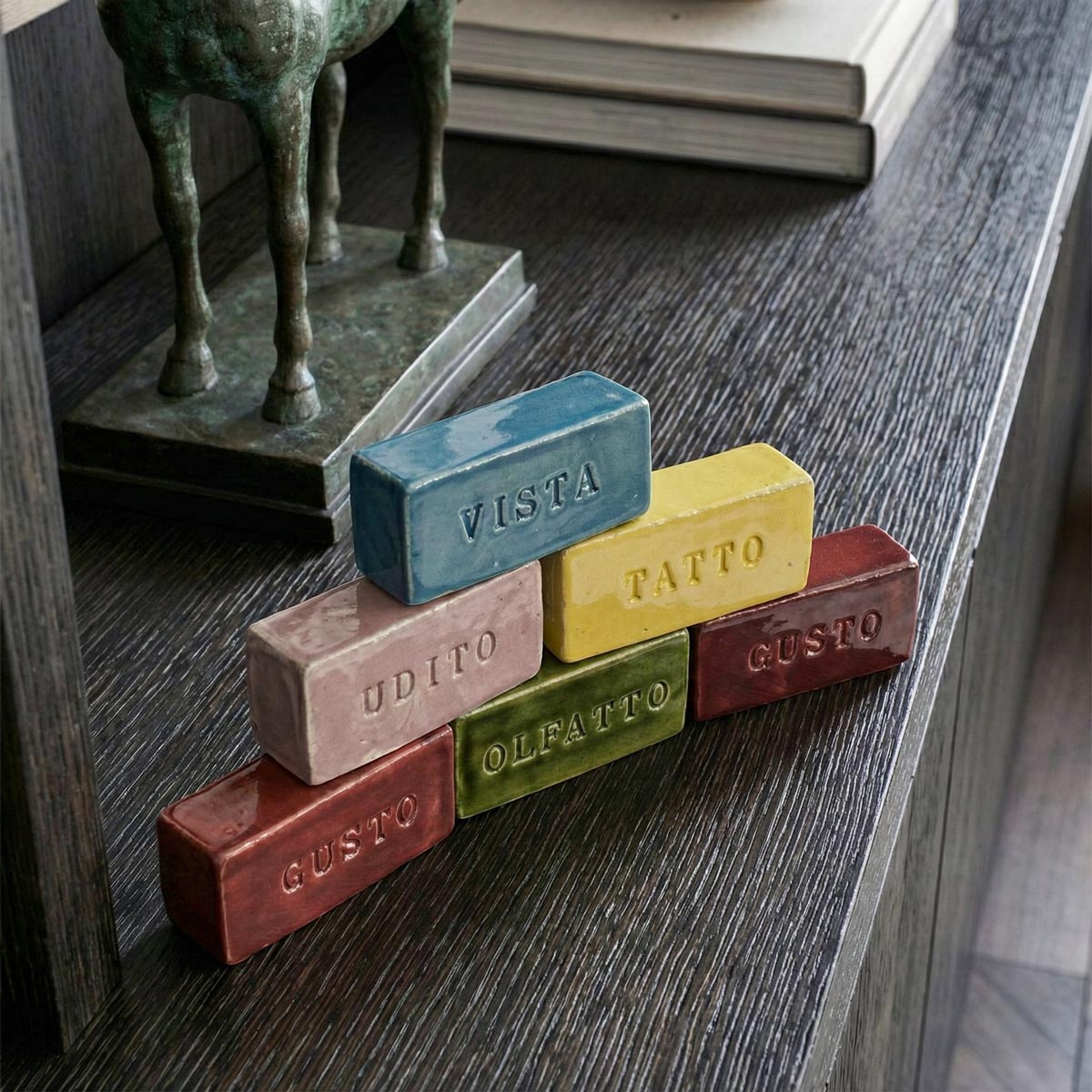 dettaglio dall'alto delle Le cinque Sculture dei Sensi disposte a piramide su unalibreria in legno scuro