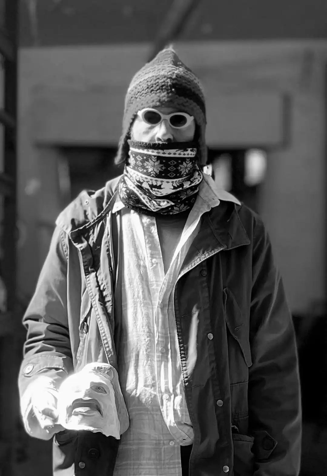 Ritratto artistico di Uodi (Emiliano Dalle Piagge) con il volto coperto e abbigliamento urbano, che regge una maschera bianca.