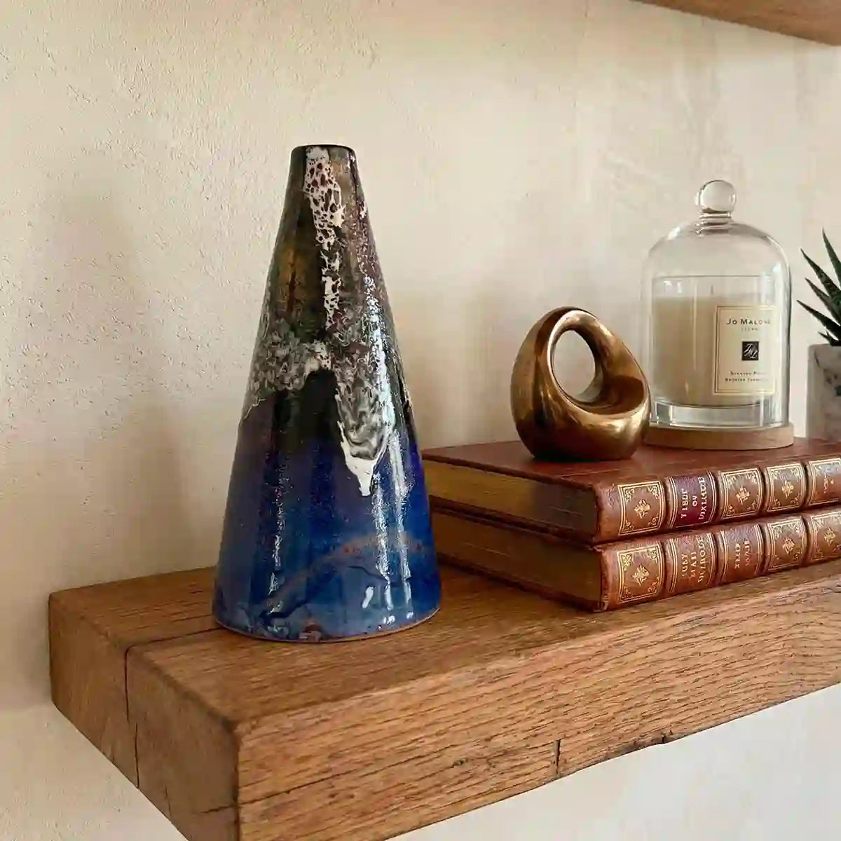 vaso conico blu su mensola di legno con libri