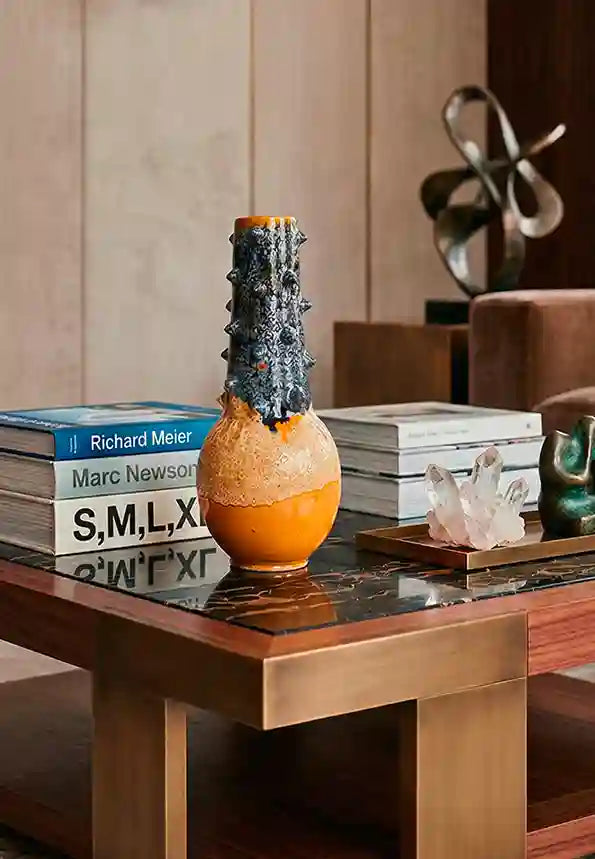 Composizione elegante da salotto: tavolino da caffè in marmo nero e legno con vaso in ceramica bicolore al centro, affiancato da libri di architettura, un cristallo grezzo e piccole sculture moderne.