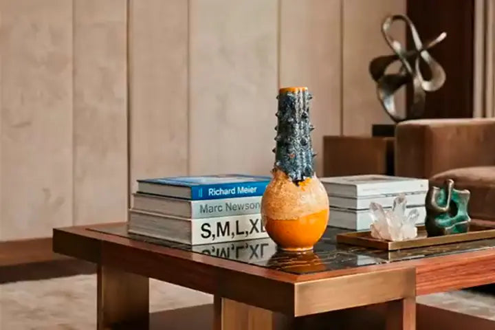 Dettaglio di arredamento d'interni di lusso: tavolino da caffè con ripiano in marmo, libri di design, cristalli decorativi e un vaso contemporaneo.