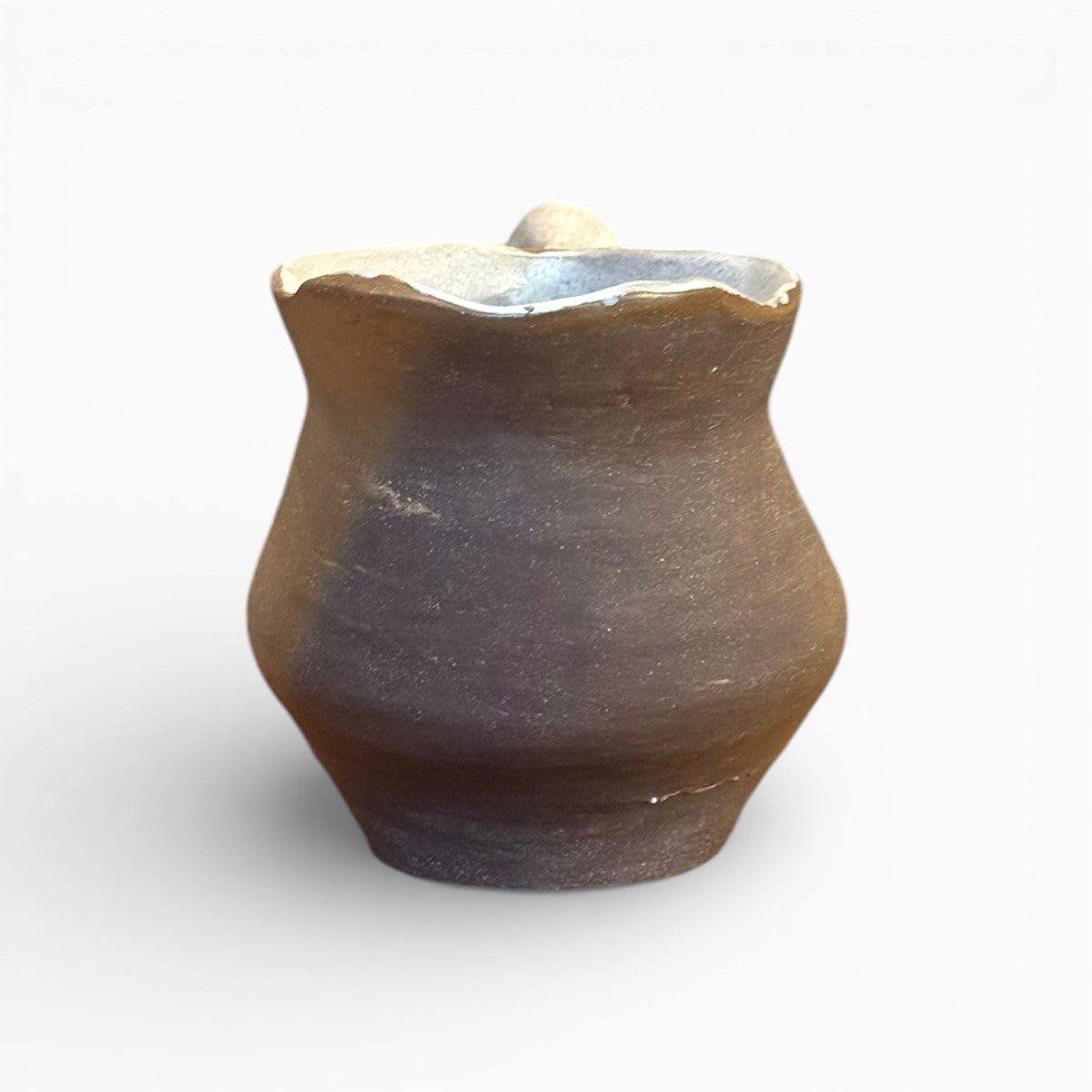Brocca artistica utilizzata come vaso minimalista su un tavolo in legno scuro.