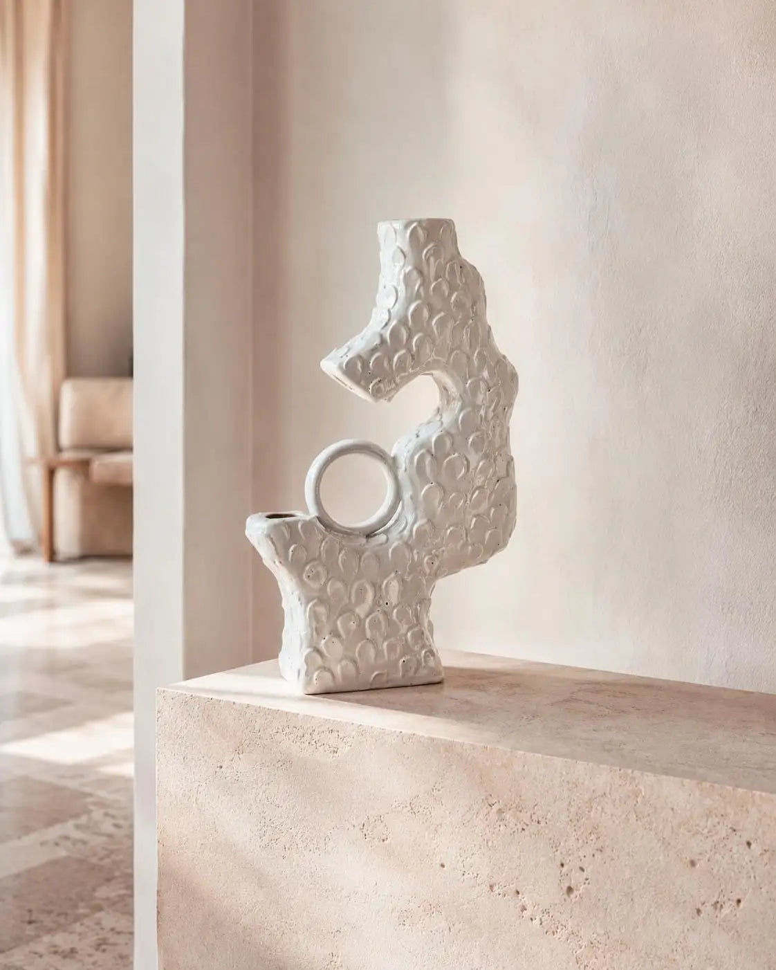 vaso scultoreo in ceramica smaltata bianca, sopra mensola in marmo, in un living di design