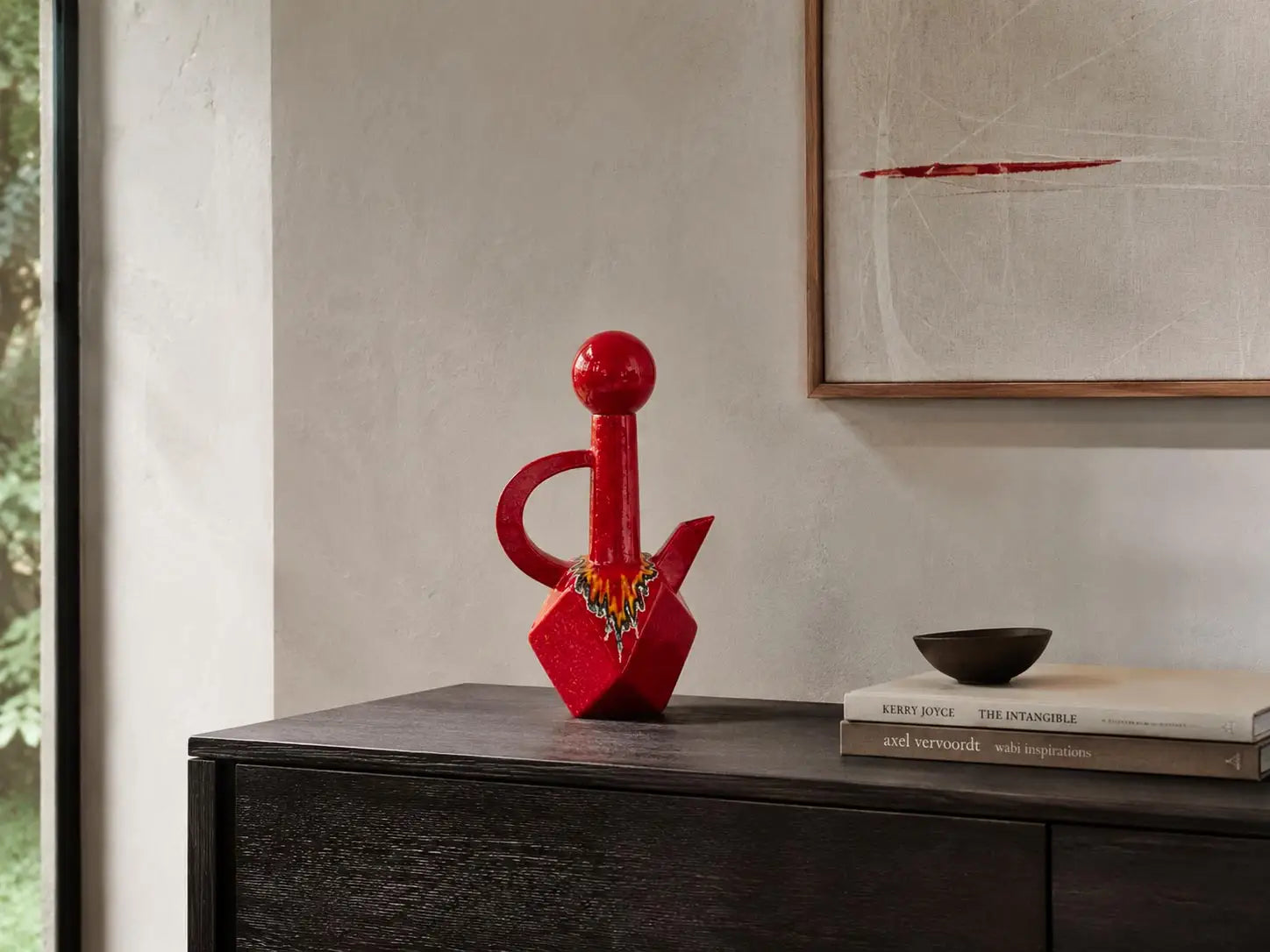 vaso brocca decorativo smaltato rosso crea un contrasto cromatico su consolle nera di deign in ambiente moderno